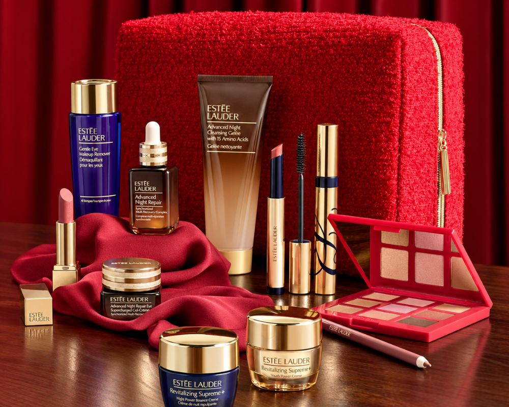 A luxury beauty gift set arranged on a dark wooden table against a deep red curtain backdrop. The set includes Estée Lauder products such as the Advanced Night Repair serum, and Advanced Night Repair Eye Gel and more