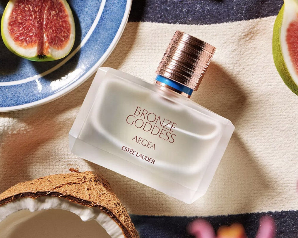 Estee Lauder Bronze Goddess Aegea Eau De Parfum with coconut & figs displayed with it on beach towel