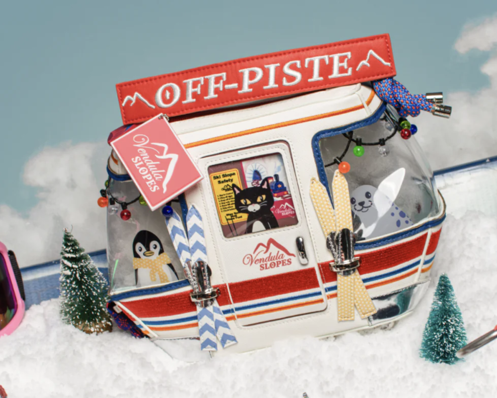 A novelty clear plastic bag shaped like a snow gondola, labeled 'OFF-PISTE' and 'Vendula Slopes,' decorated with penguin and cat stickers, set in a snowy miniature scene.
