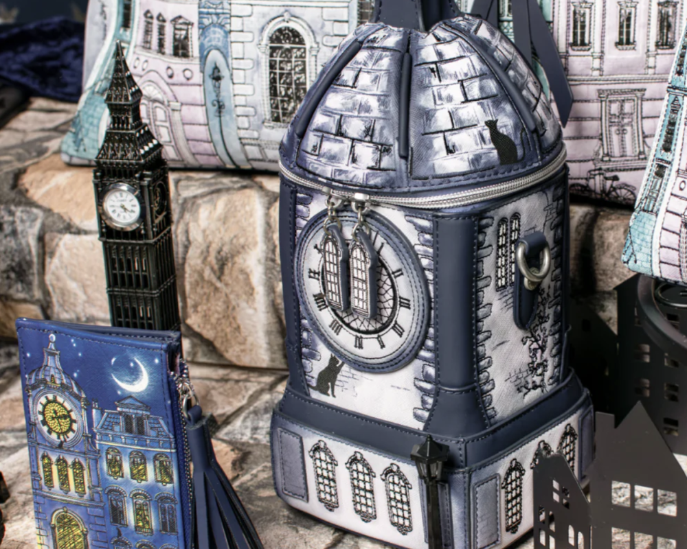 A gothic London-themed zippered bag shaped like Big Ben, displayed alongside matching zippered accessories including a blue clock-face notebook and a black cutout streetlamp on a stone surface.