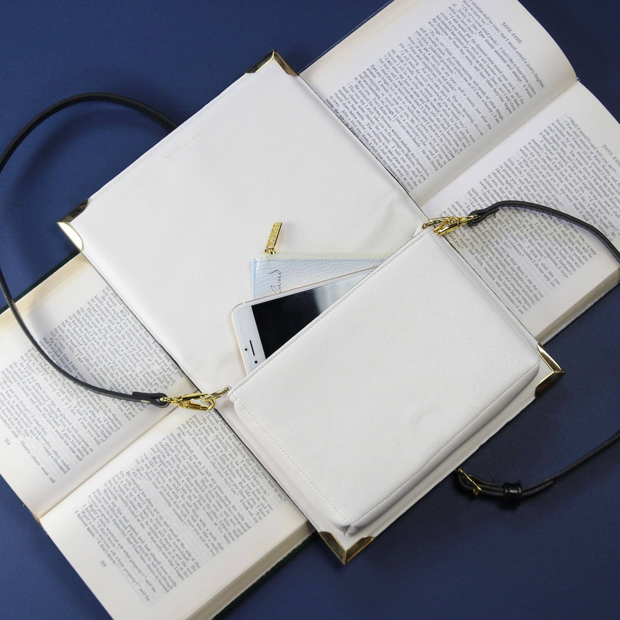 White purse bag with phone inside on open book against a blue background