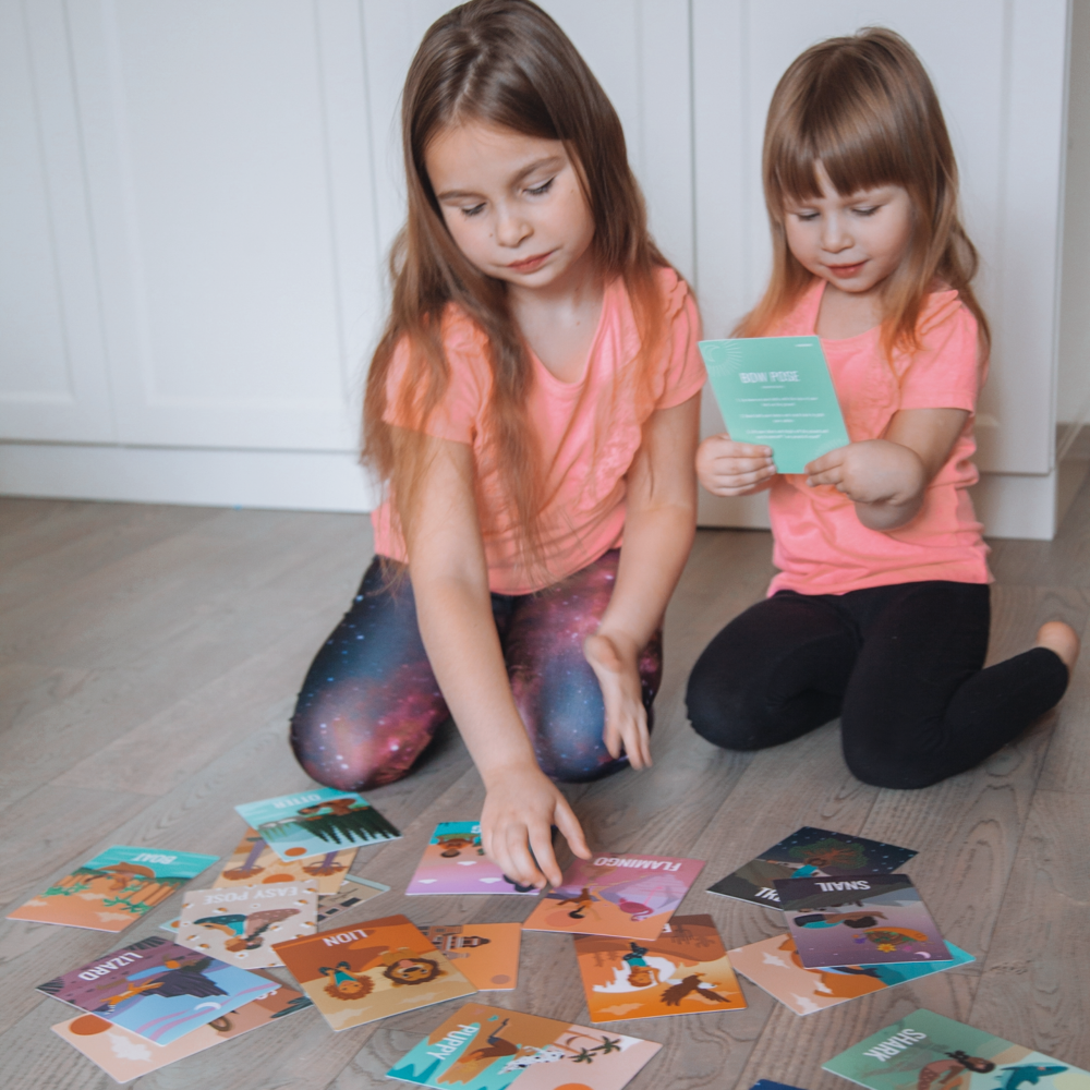 Two young girls playing with colorful cards on a wooden floor.