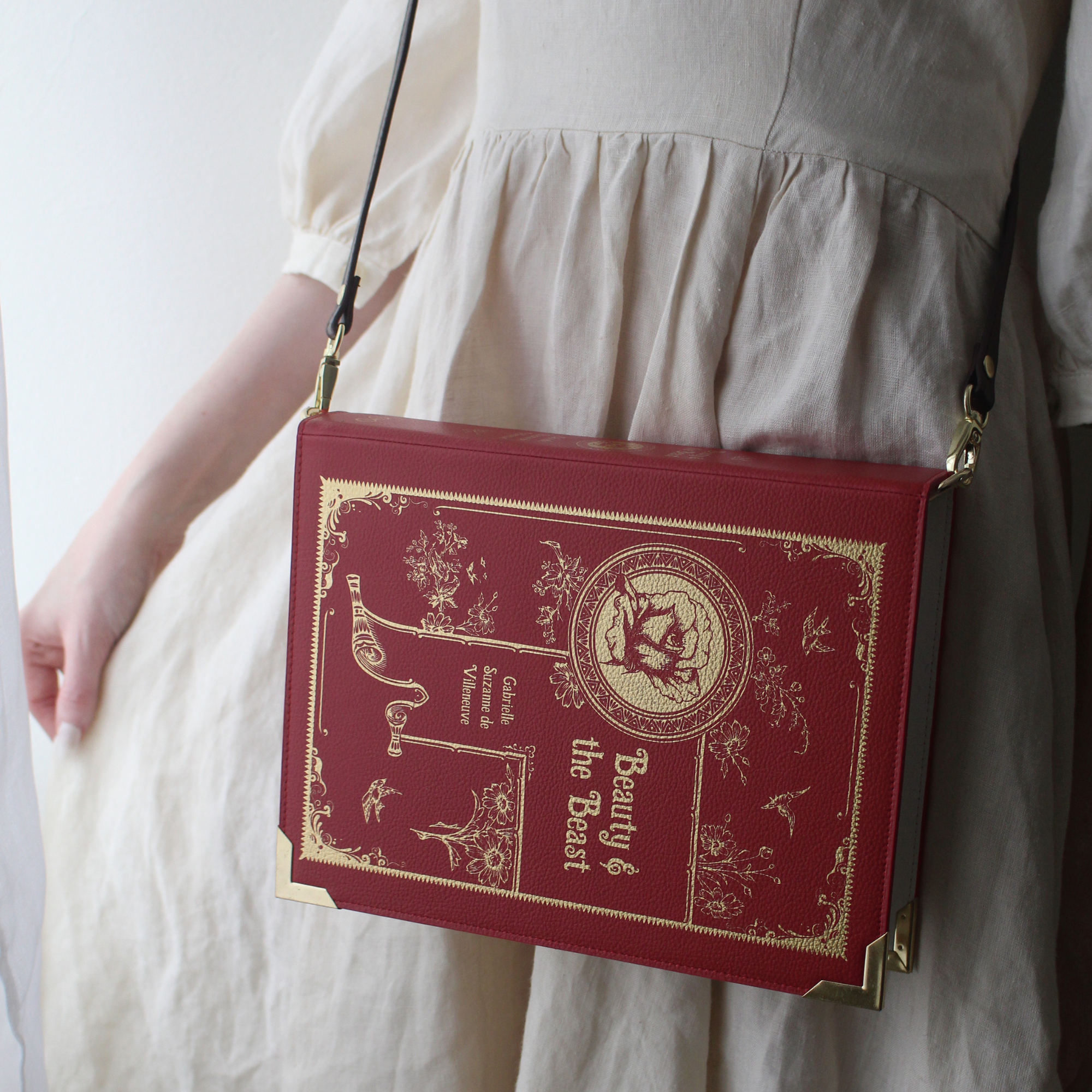A red faux-leather crossbody bag designed to look like a vintage 'Beauty & the Beast' book