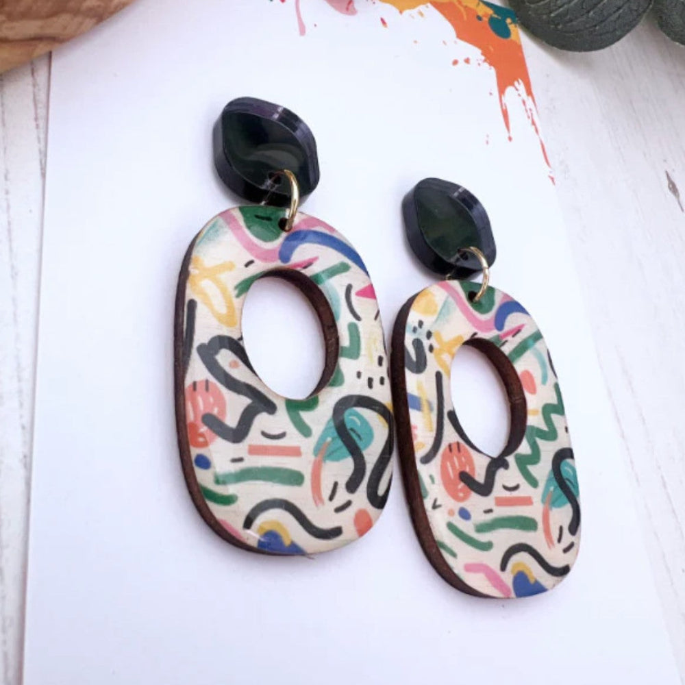 Colorful abstract patterned earrings on a white background with paint splashes.