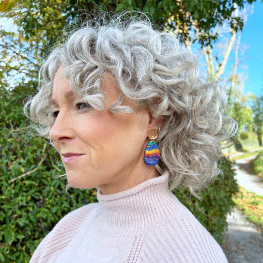 Person with curly gray hair wearing colorful earrings outdoors