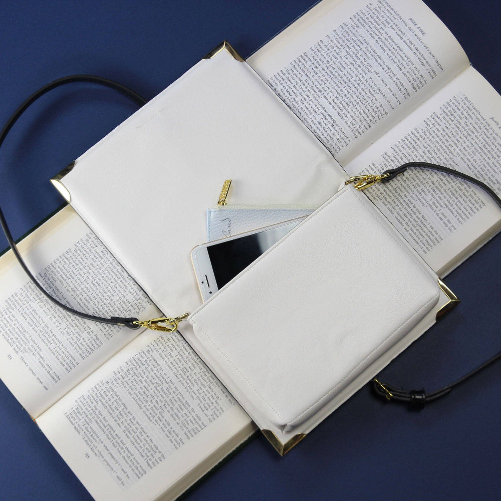 White handbag with phone compartment on top of an open book