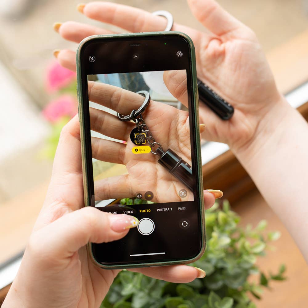 Person taking a photo of a keychain with a phone, with a blurred background