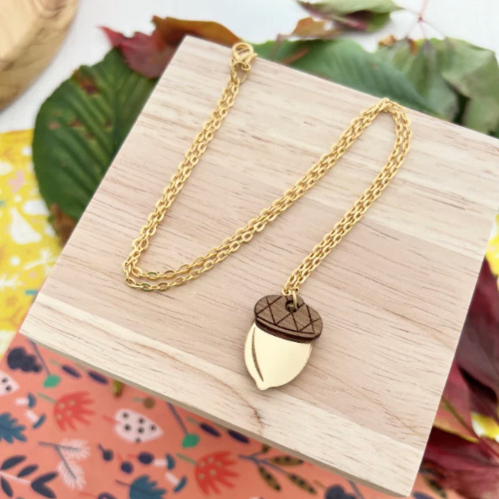 Gold necklace with a leaf-shaped pendant on a wooden box with a colorful floral background