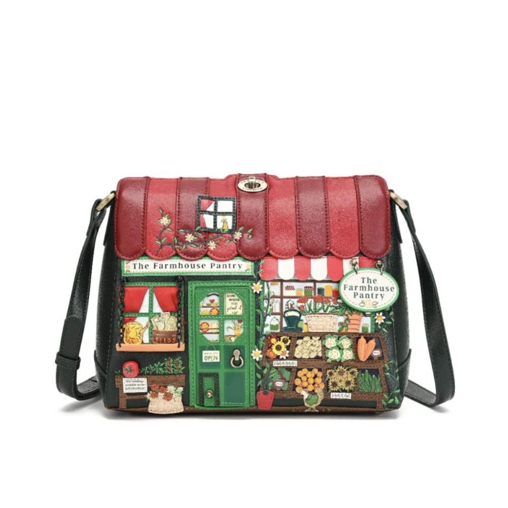 A dark green leather shoulder bag featuring a highly detailed, colourful patchwork design of a farm market storefront with red awnings, green doors, and various produce and flower illustrations. The bag has a top flap, a black shoulder strap, and a small gold clasp at the top.