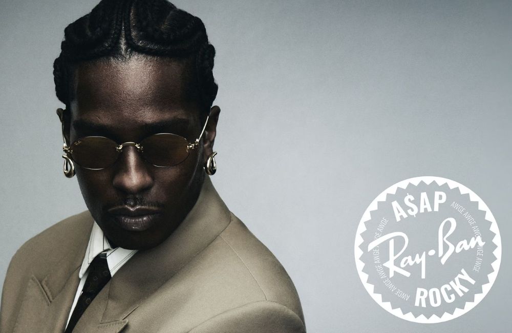 A portrait of ASAP Rocky wearing gold-toned Ray-Ban sunglasses, a beige suit jacket, and a white shirt.
