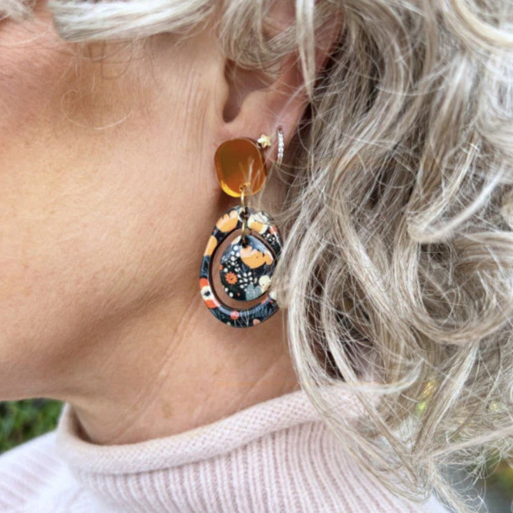 Close-up of a person wearing a colorful earring with an orange bead.
