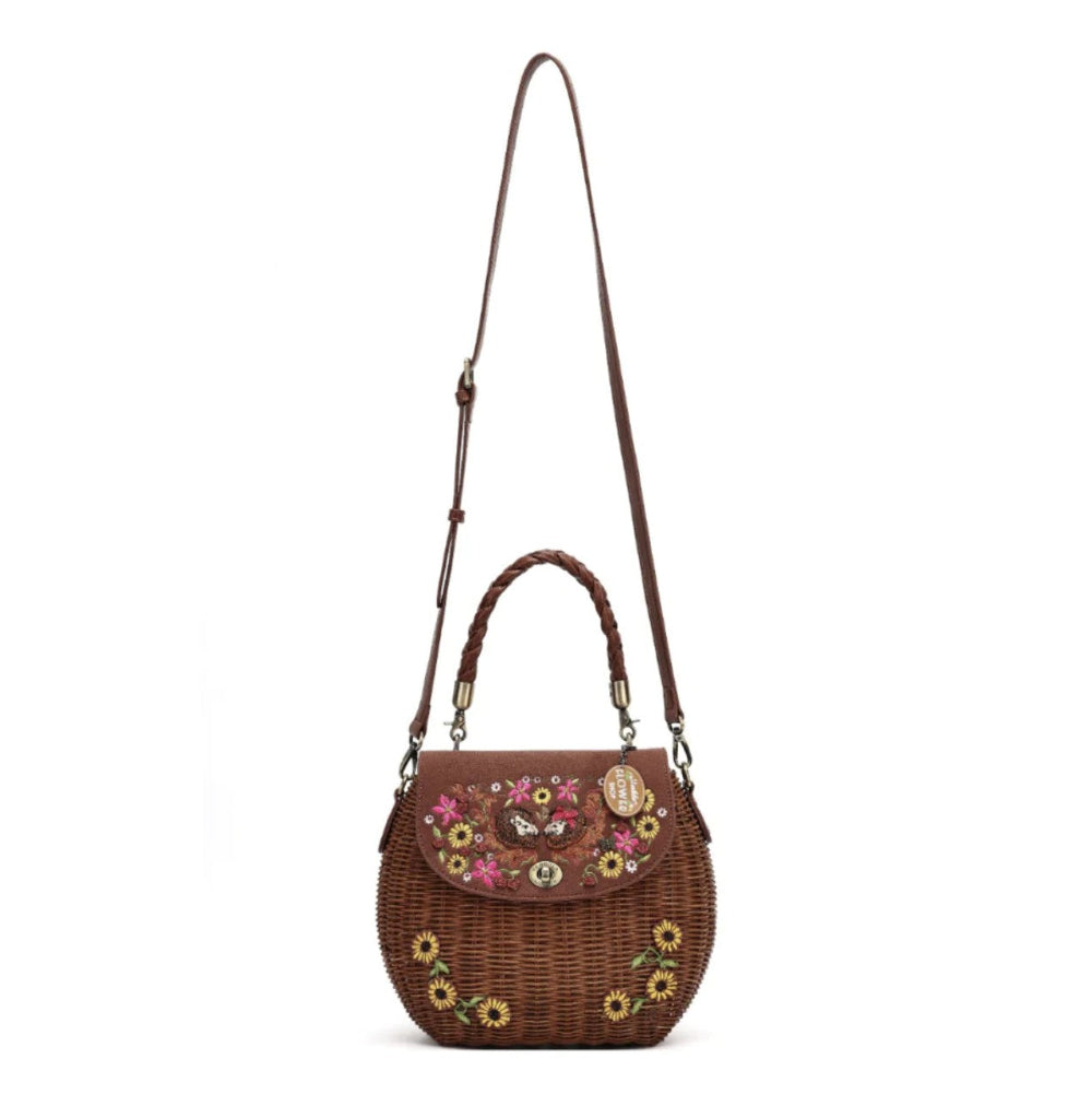 A brown woven wicker shoulder bag with a top handle, a long adjustable shoulder strap, and colorful floral embroidery on the front flap and lower body. The bag is shown against a plain white background.