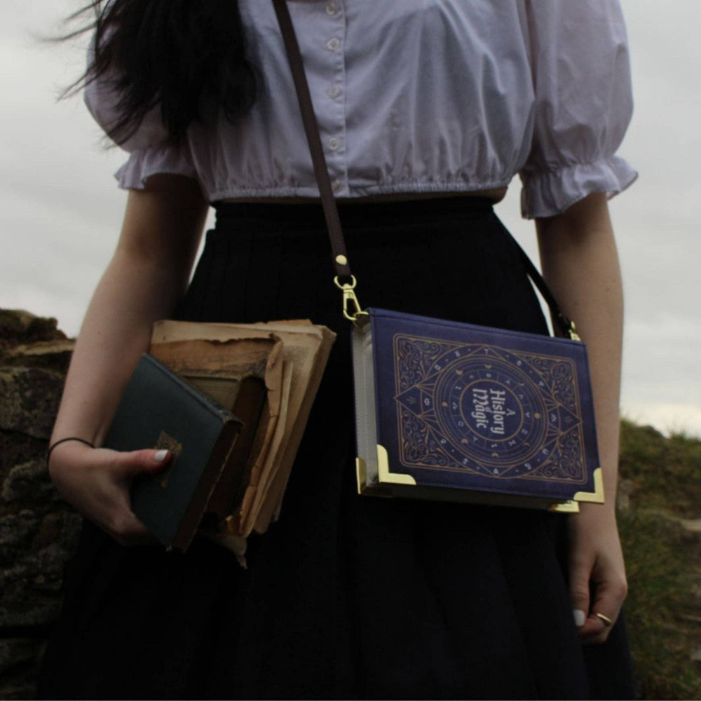 Person holding books and a blue leather-bound book with gold embossing outdoors.
