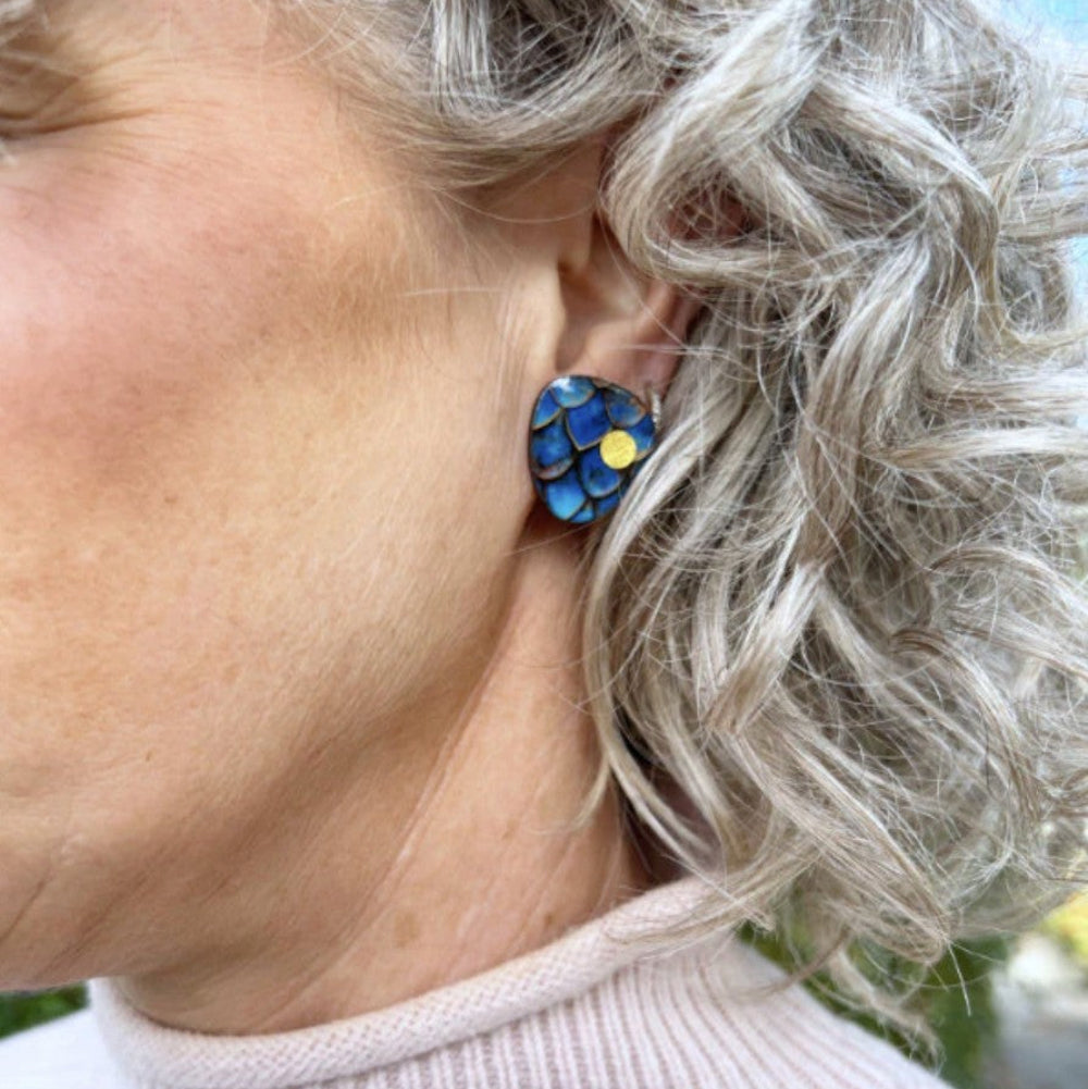 Close-up of a person wearing a blue floral earring with a yellow center.
