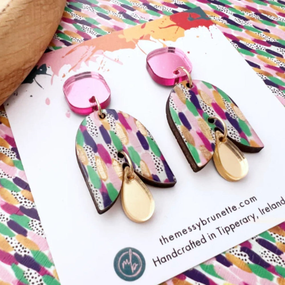 Colorful earrings on a branded card with a multicolored patterned background