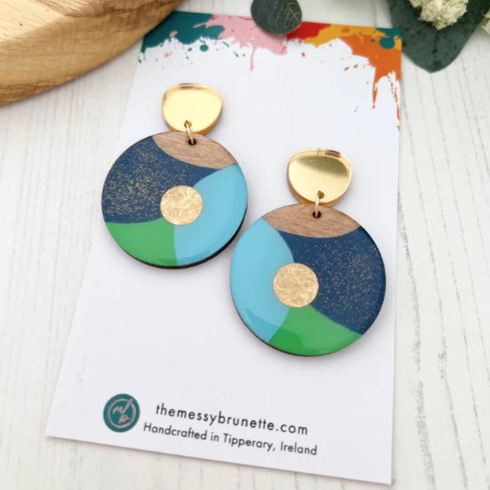 Colorful earrings on a branded card with a wooden surface and flowers in the background