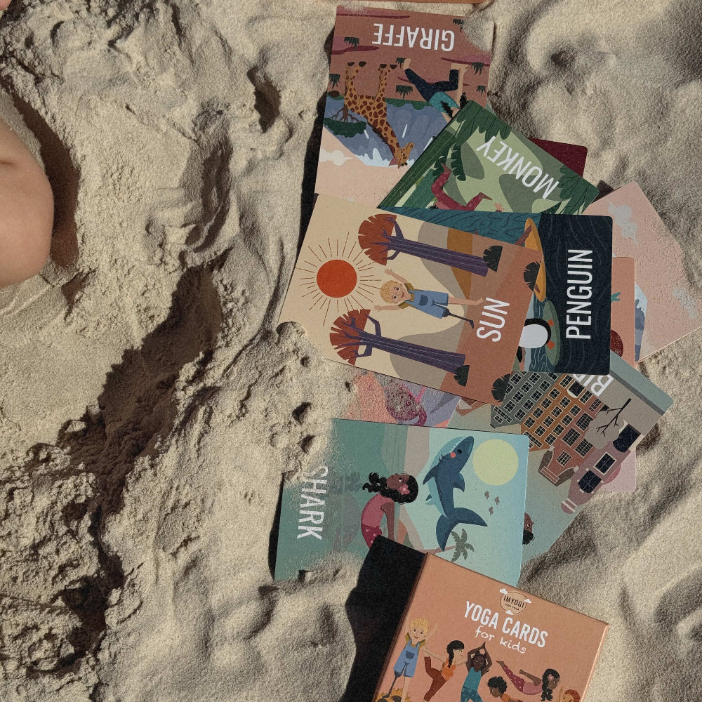Collection of colorful yoga cards on sand with a box labeled 'Girlfist'.