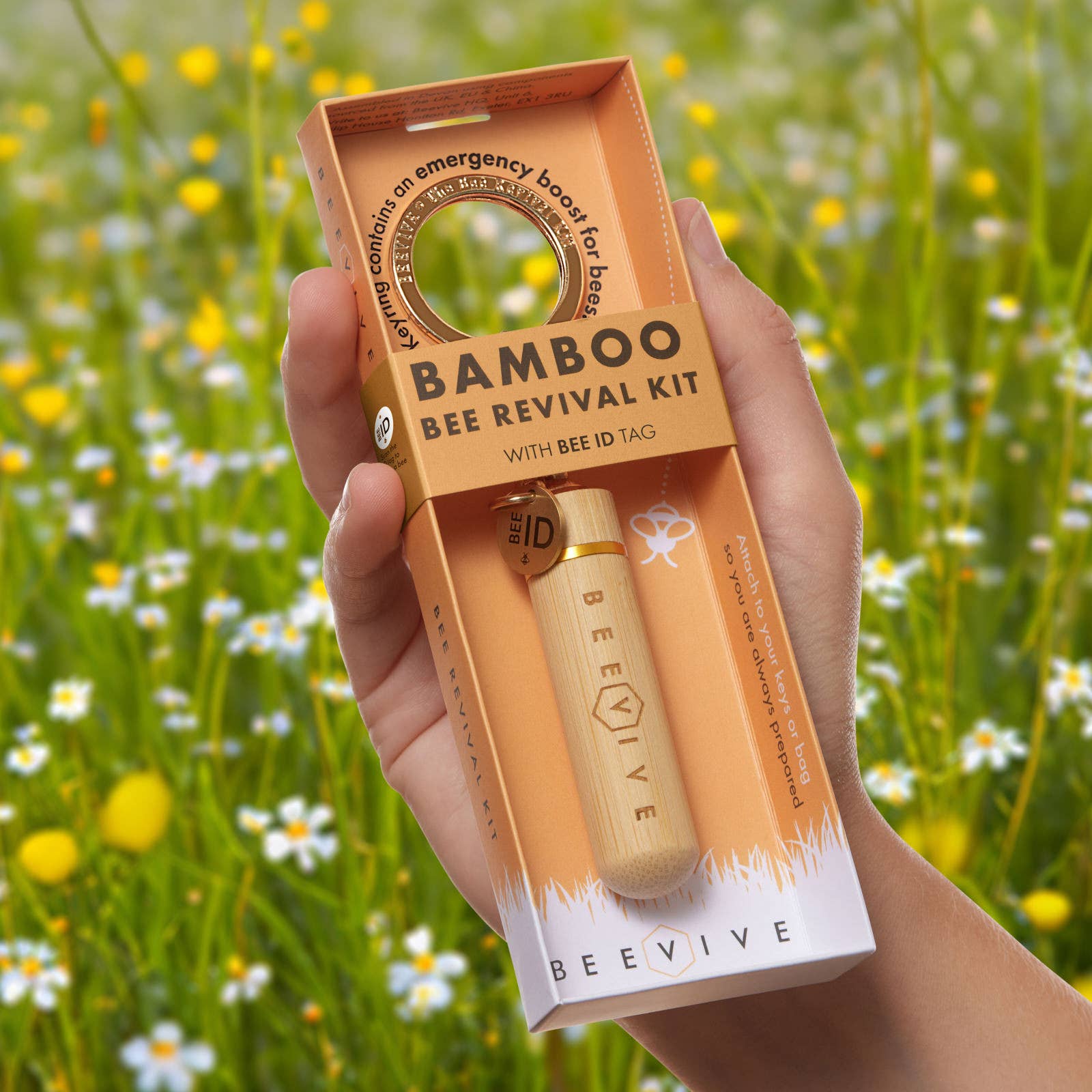 Hand holding a Bamboo Bee Revival Kit with a natural background of green grass and flowers.