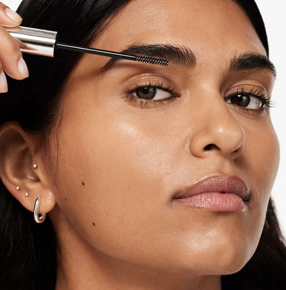 Woman applying brow gel to her eyebrows with a close-up focus on her face.
