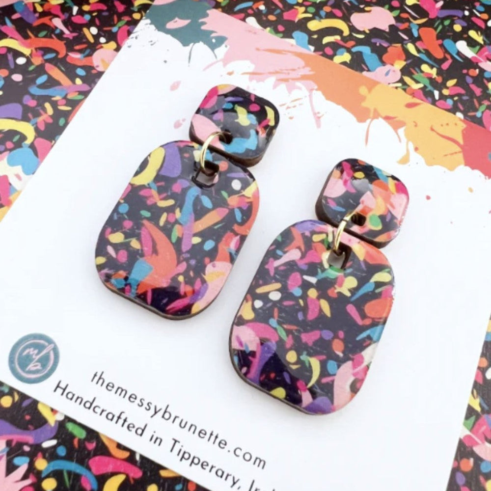 Colorful abstract patterned earrings on a colorful background with 'the messy brunette' branding.