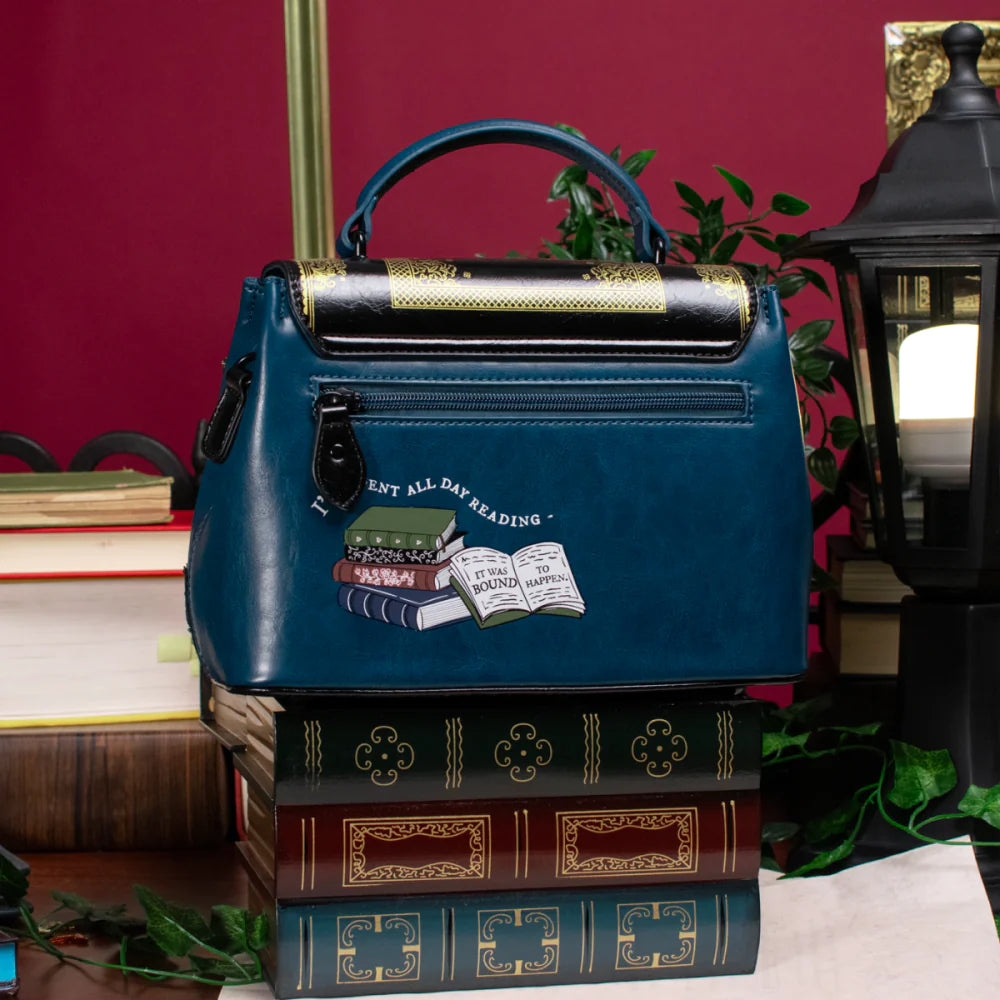 Blue handbag with book-themed design on a stack of books against a red wall.