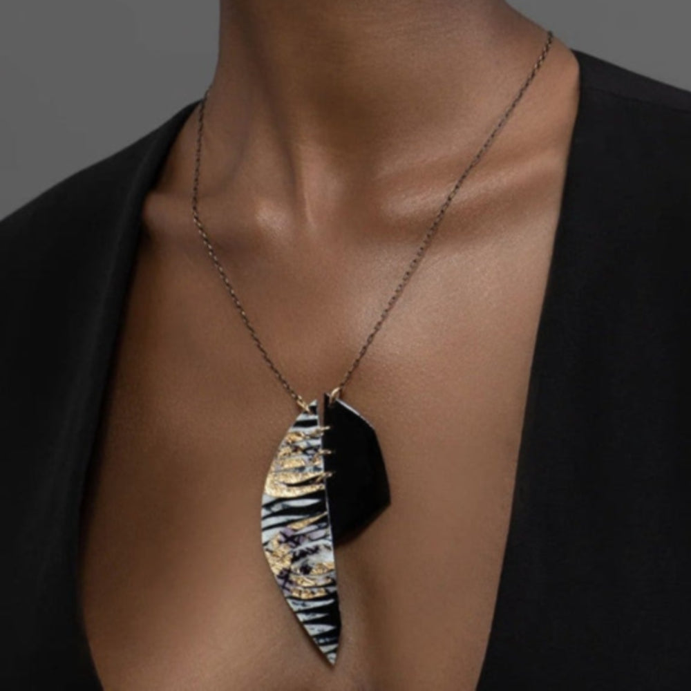 Woman wearing a black top with a unique necklace against a gray background