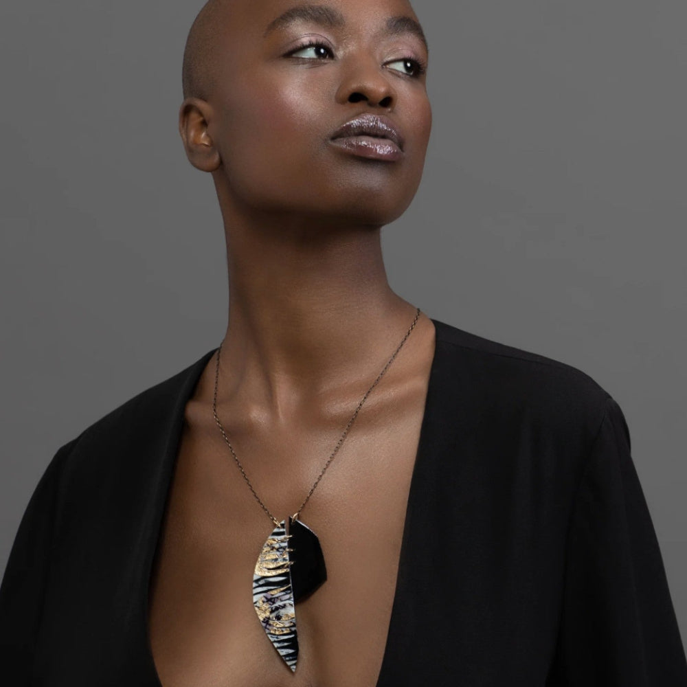 Woman wearing a black top with a unique necklace against a gray background