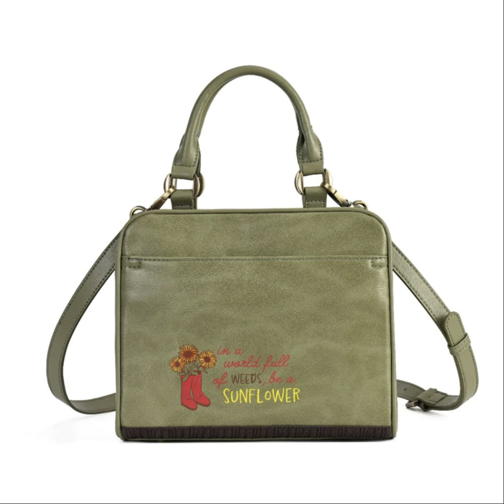 An olive green faux-leather handbag with a top handle, adjustable shoulder strap, and a front pocket featuring a red and yellow embroidered design with the text 'In a world full of weeds, be a SUNFLOWER' alongside red rain boots and sunflowers.