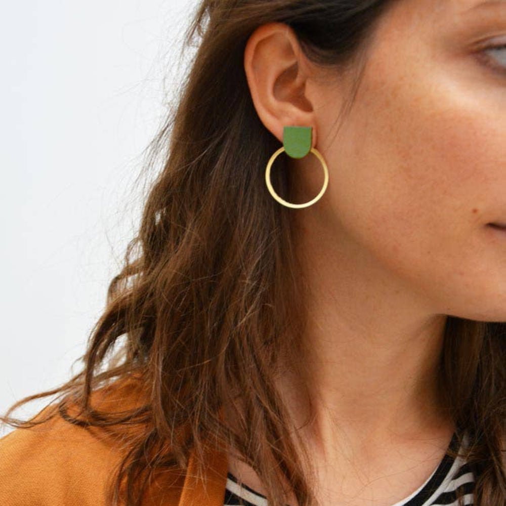 Close-up of a person wearing gold hoop earrings with green heart charms.