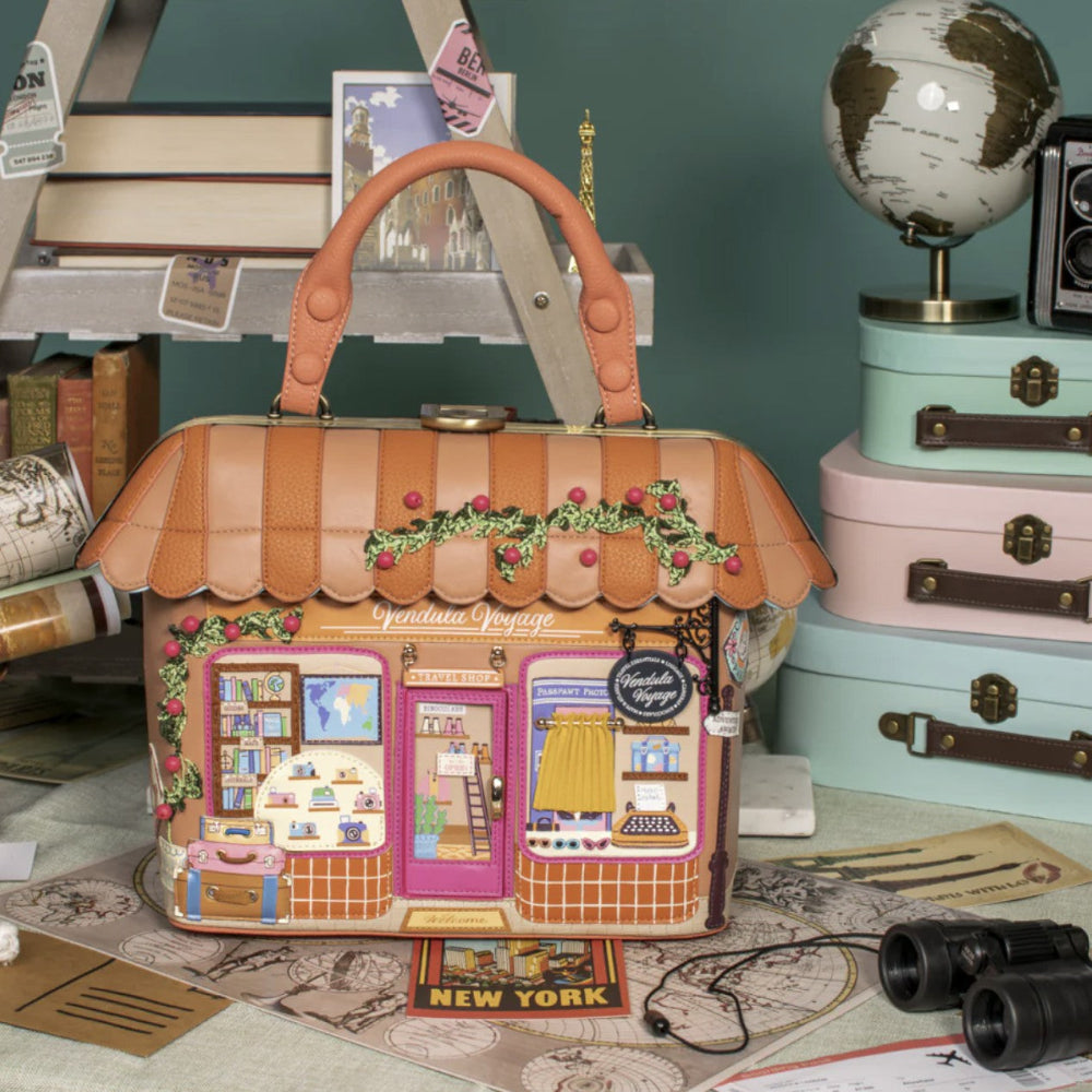 Decorative handbag designed like a small store with books and travel items in the background