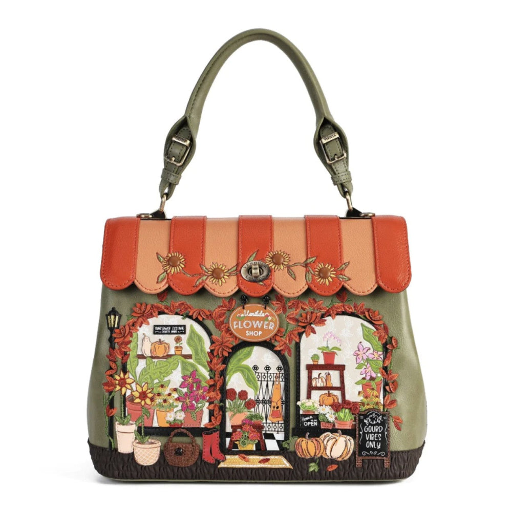 An olive green handbag with a scalloped orange and beige leather top flap, decorated with autumn-themed embroidery featuring a flower shop, pumpkins, and flowers.