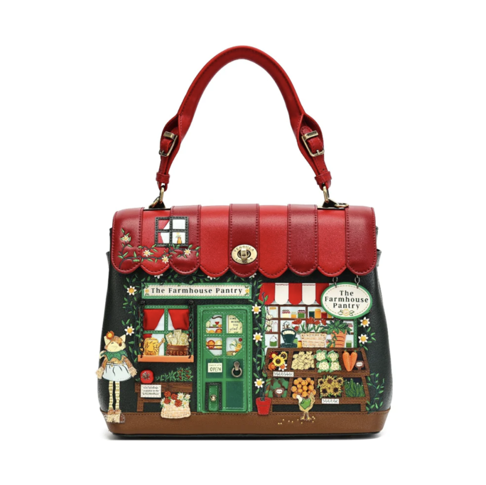 A structured handbag with a red leather top handle and flap, featuring a detailed illustration of a farmhouse pantry storefront on the front. The bag has a red top section, a dark green illustrated facade, and a brown base, photographed against a solid white background.