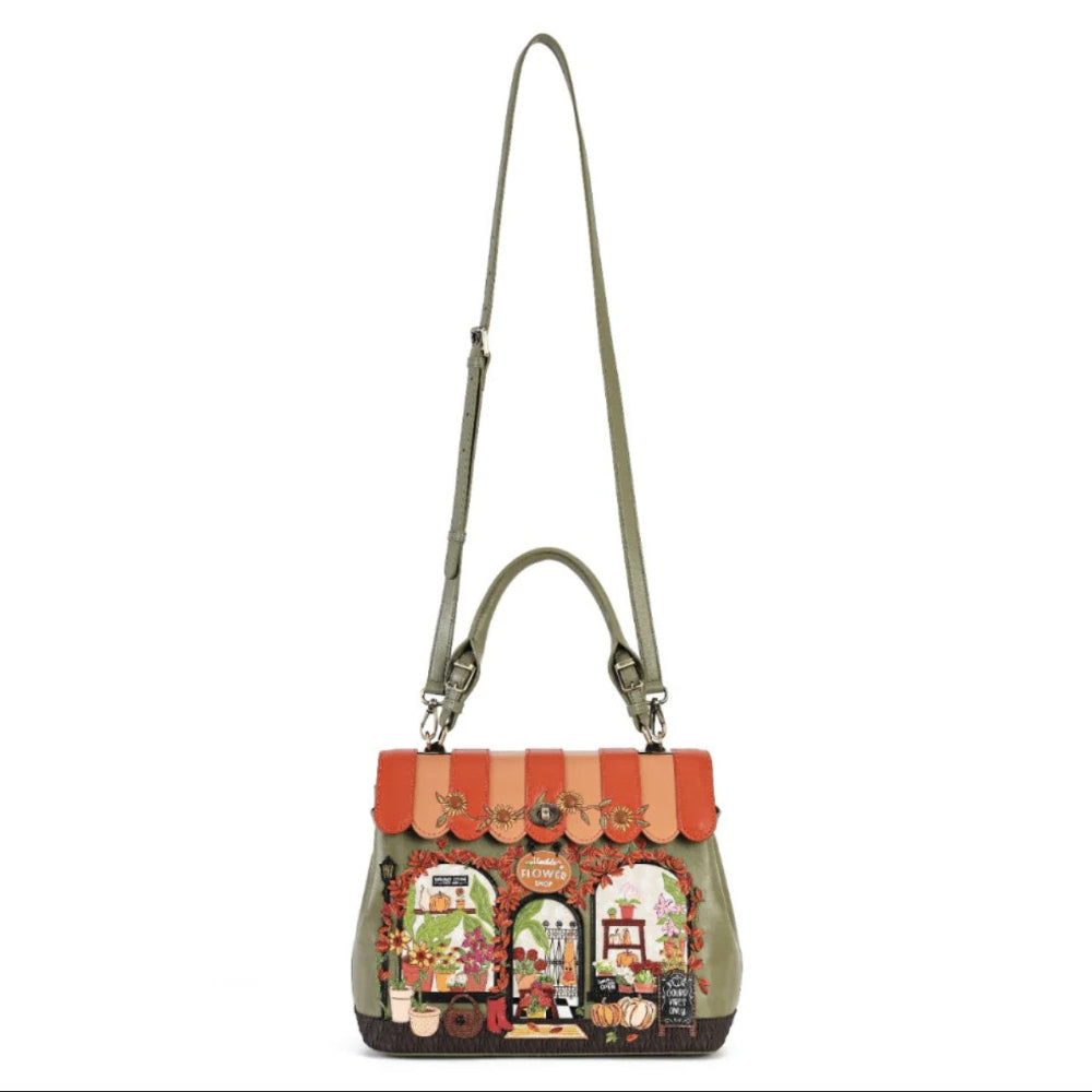 An olive green leather shoulder bag featuring a detailed, colorful embroidered market scene on the front flap, complete with a striped awning in orange and beige.