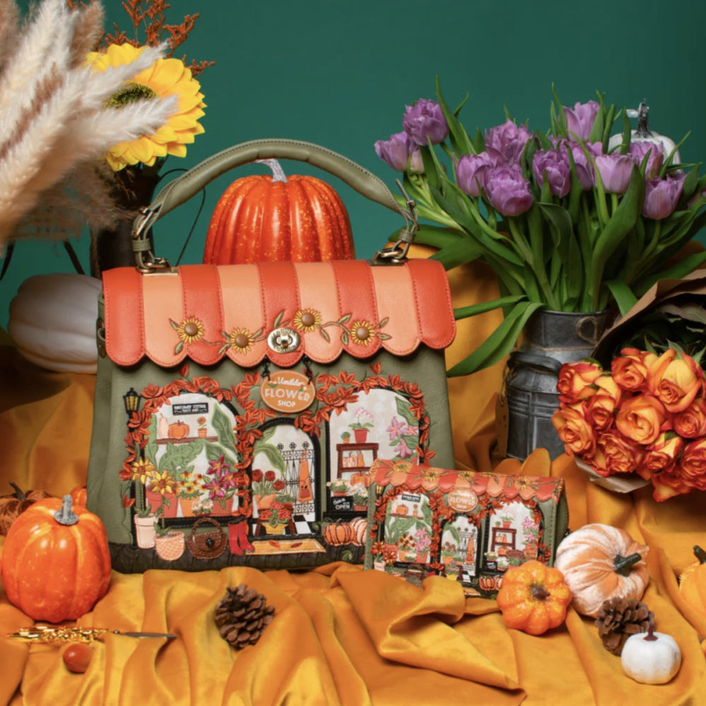 An autumn-themed handbag styled with pumpkins, tulips, and fabric on a teal background. The bag has a green body, a peach and orange scalloped roof, and detailed vintage-style storefront graphics on the front.