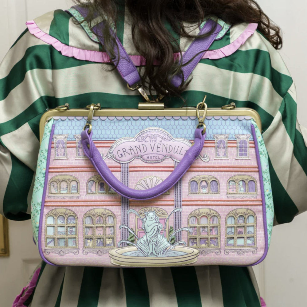 Handbag with architectural design and 'Grand Vendul Hotel' text, held by a person in a striped shirt.