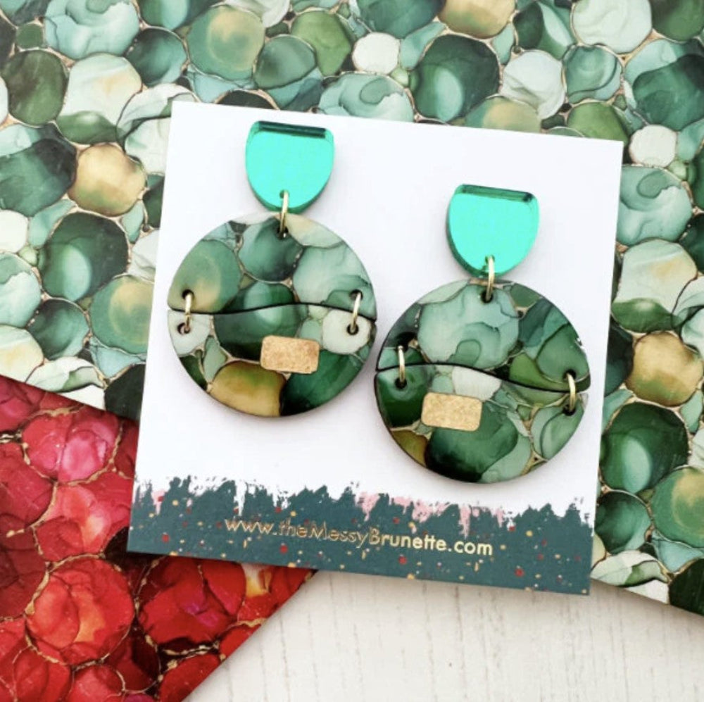 Green and gold earrings on a branded card with a colorful background