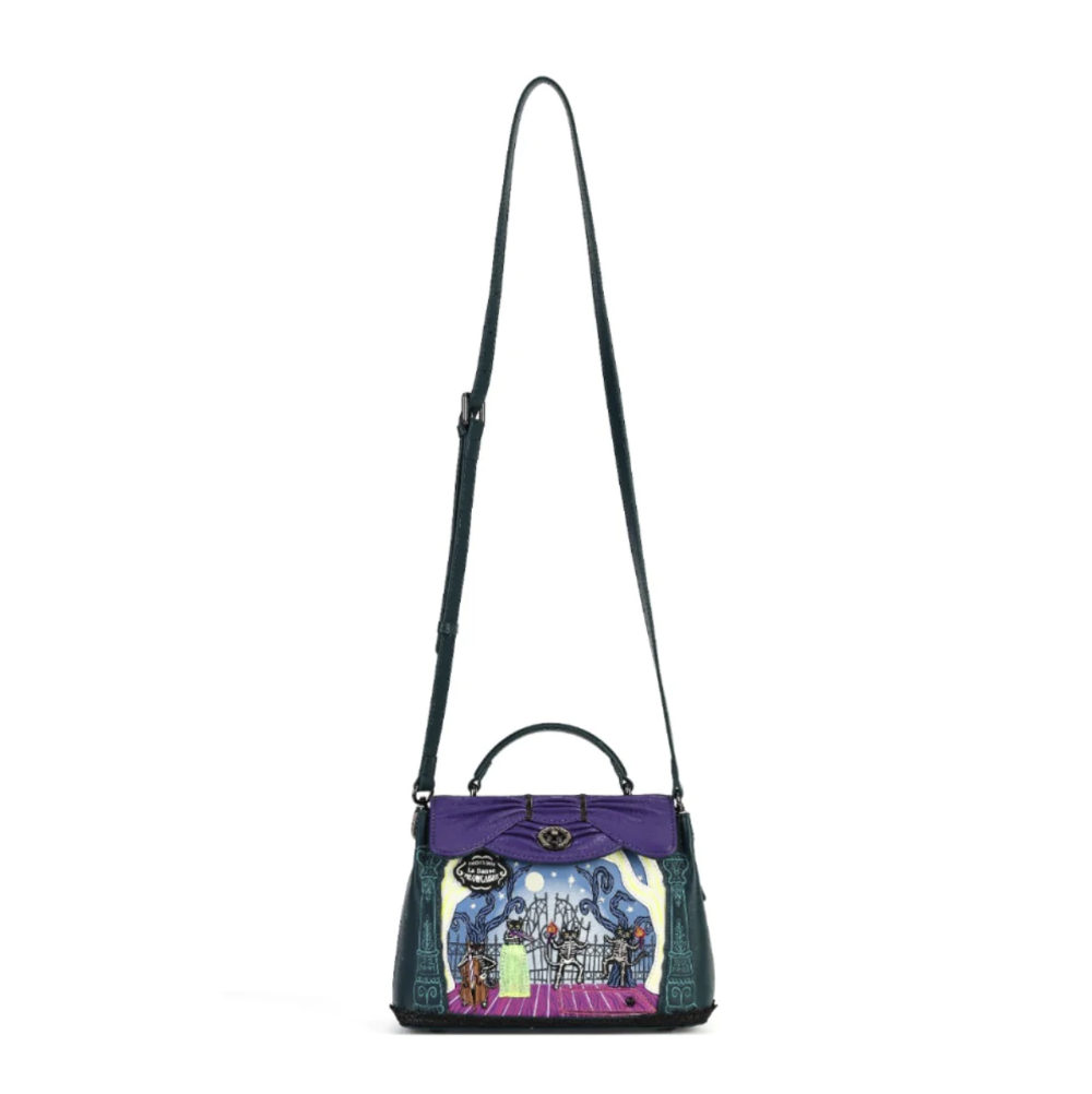 A structured handbag with a purple top flap, dark green textured leather sides, and a colorful illustrated front panel, featuring a long dark green shoulder strap on a white background.