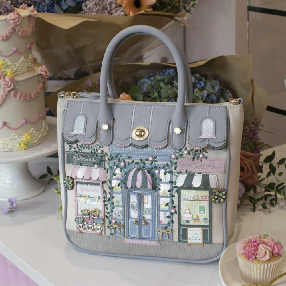 Handbag with decorative design of a quaint street shop fronts, placed on a surface with floral and cake decorations.