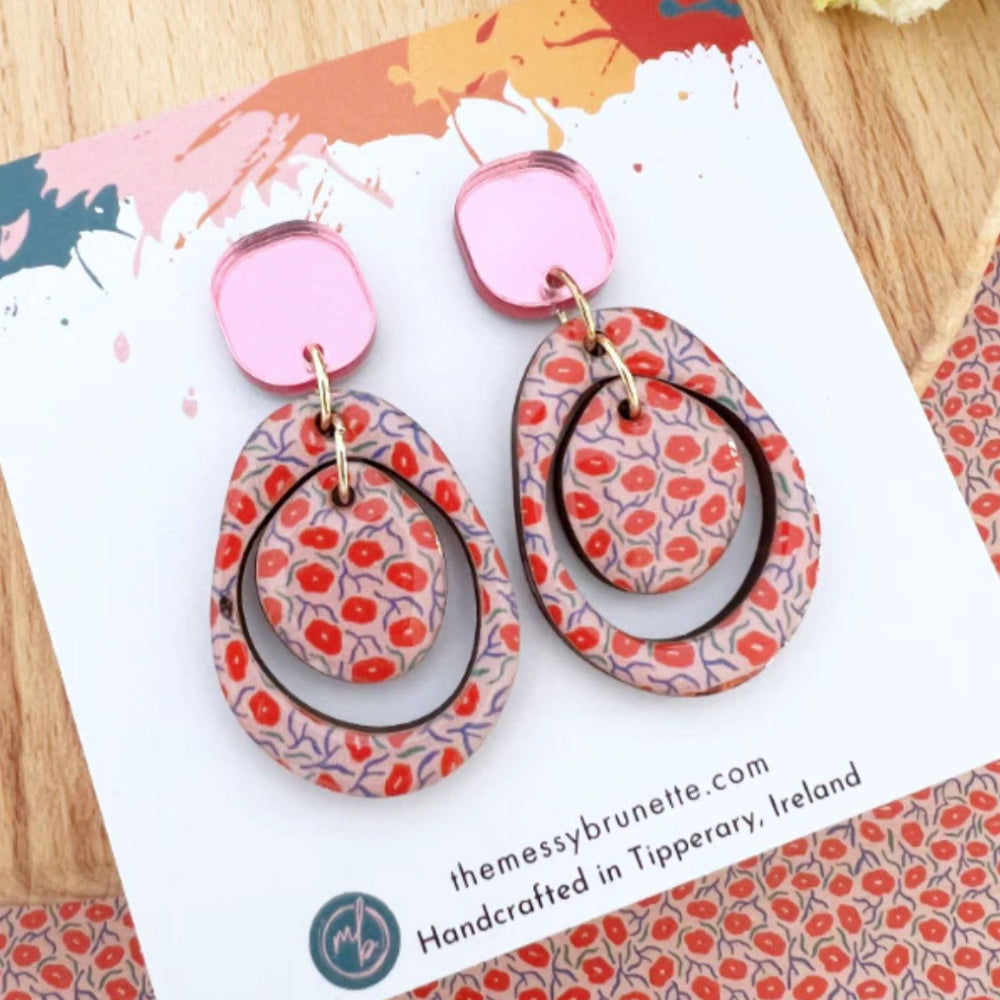 Pair of floral-patterned earrings on a branded card with a wooden surface background.