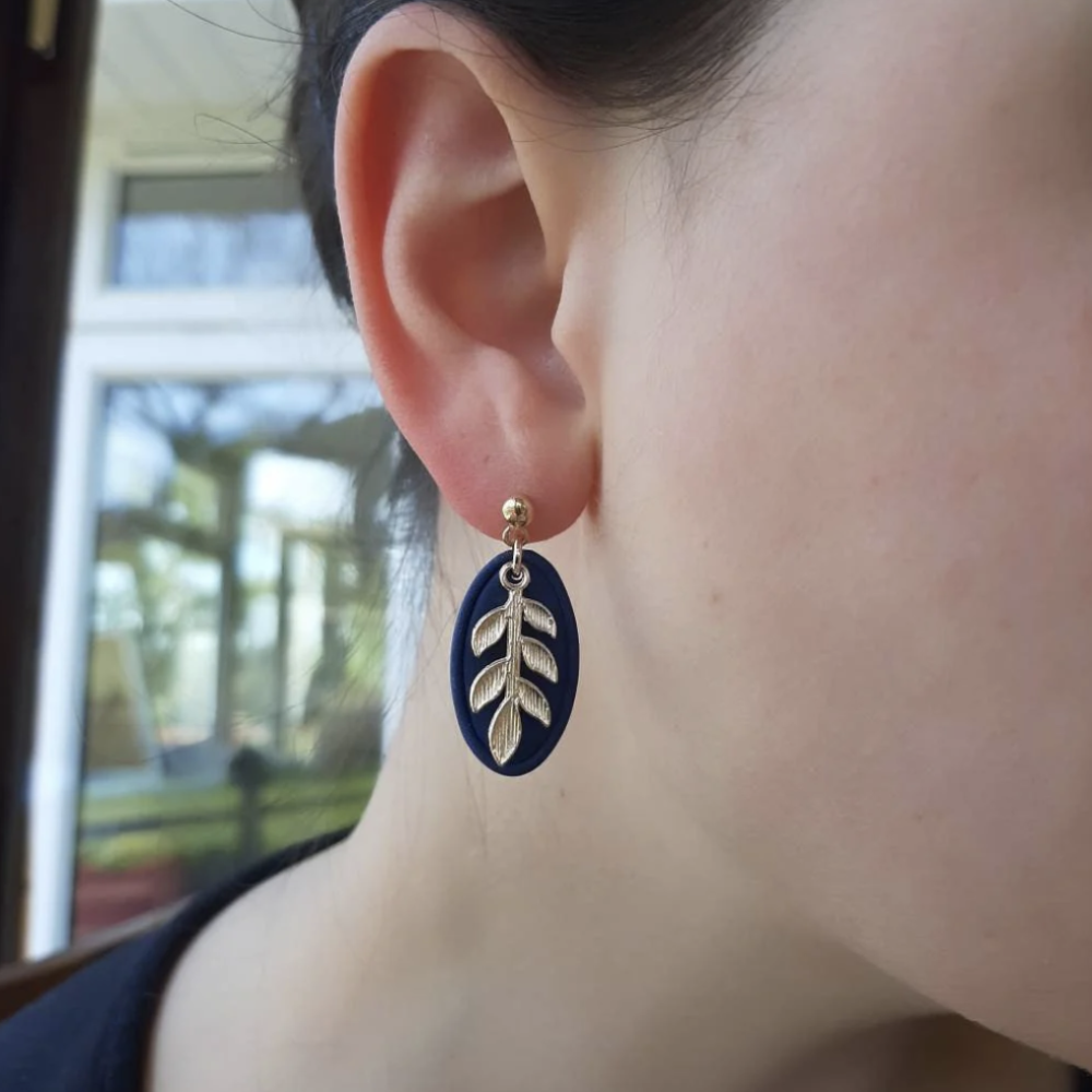 Close-up of an ear wearing a blue and gold earring with leaf design.