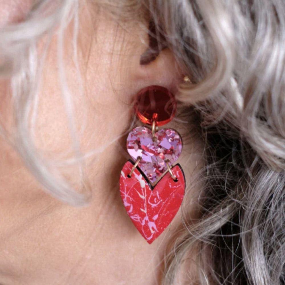 Close-up of a person wearing red heart-shaped earrings with floral details.