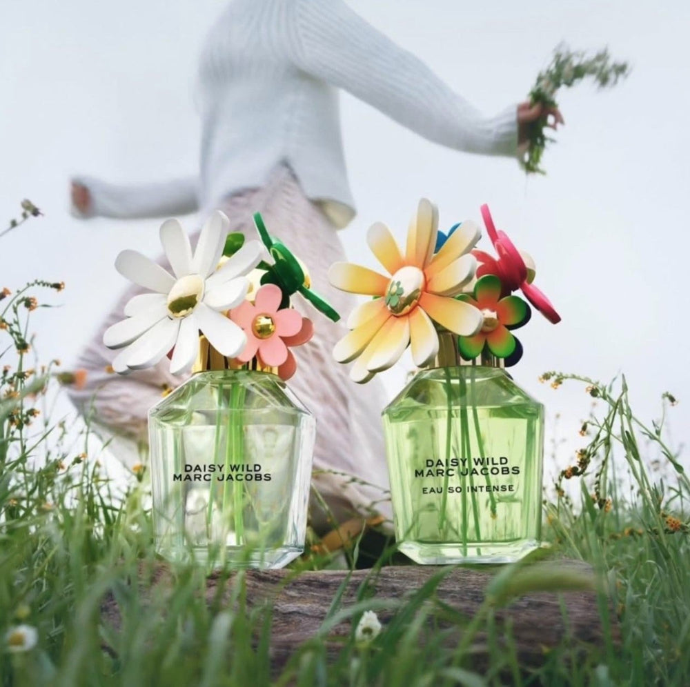 Two bottles of Marc Jacobs Daisy Wild perfume with floral designs on a grassy background.