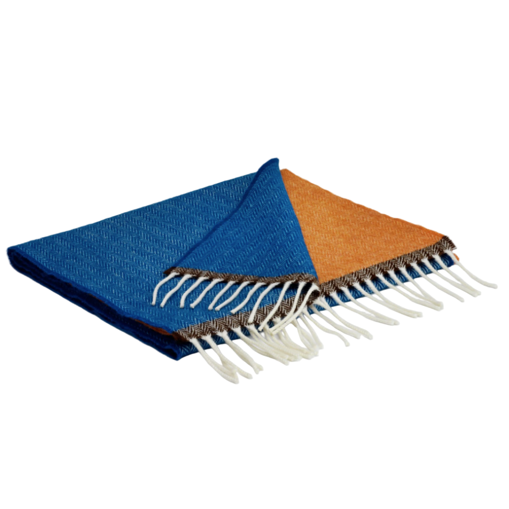 Blue and orange plaid blanket with white fringe on a light gray background