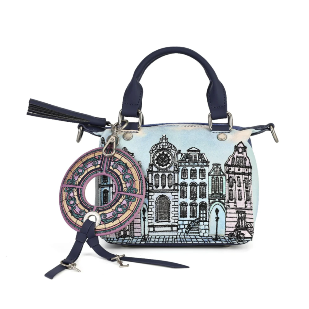 A navy blue leather handbag with a light blue and black architectural cityscape illustration on the front. It features a top handle, silver-tone hardware, a tassel charm, and a large circular decorative charm with purple and gold details.
