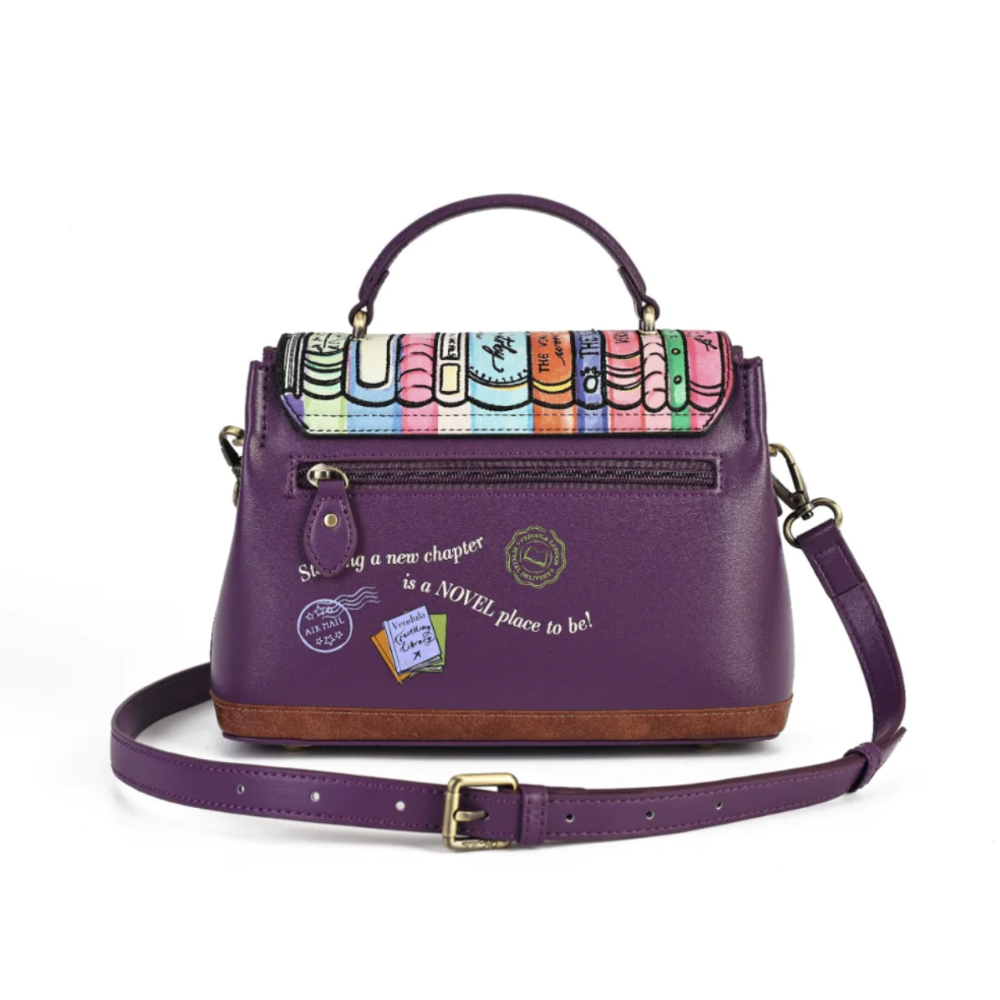 A purple leather handbag with a colorful book spine pattern on the flap, gold-tone hardware, a top handle, and an adjustable shoulder strap, shown on a white background.