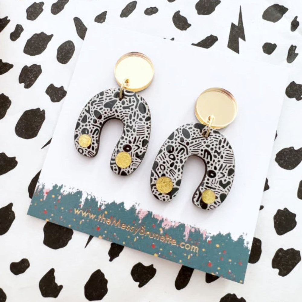 Pair of patterned earrings on a branded card with a black and white background
