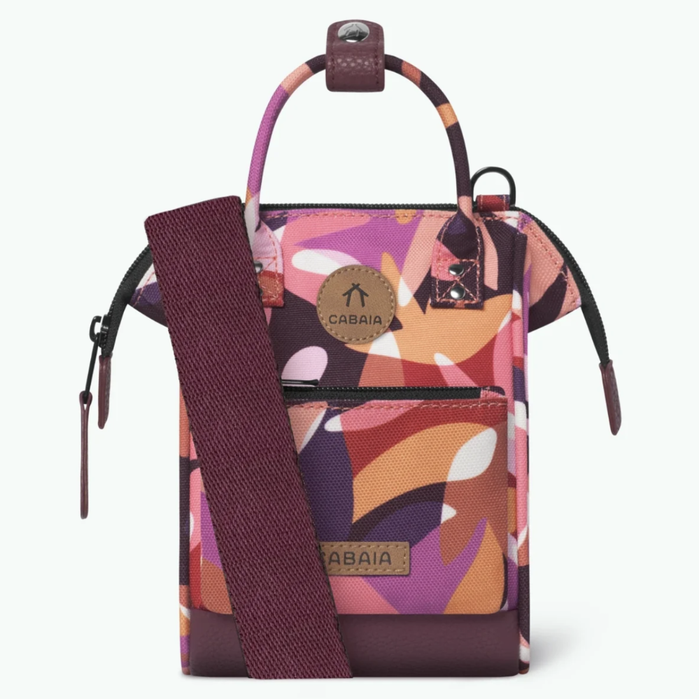 A small Cabaia crossbody bag with a colorful abstract floral pattern in pink, orange, purple, and white, featuring a burgundy shoulder strap and a circular logo patch on the front pocket.