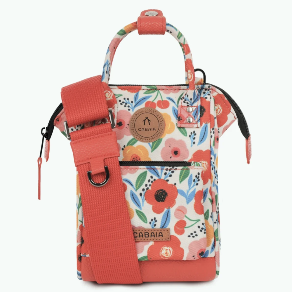A Cabaía brand floral tote bag with a coral red adjustable shoulder strap, coral red base, and a white background covered in a colorful floral print of red, orange, and blue flowers.