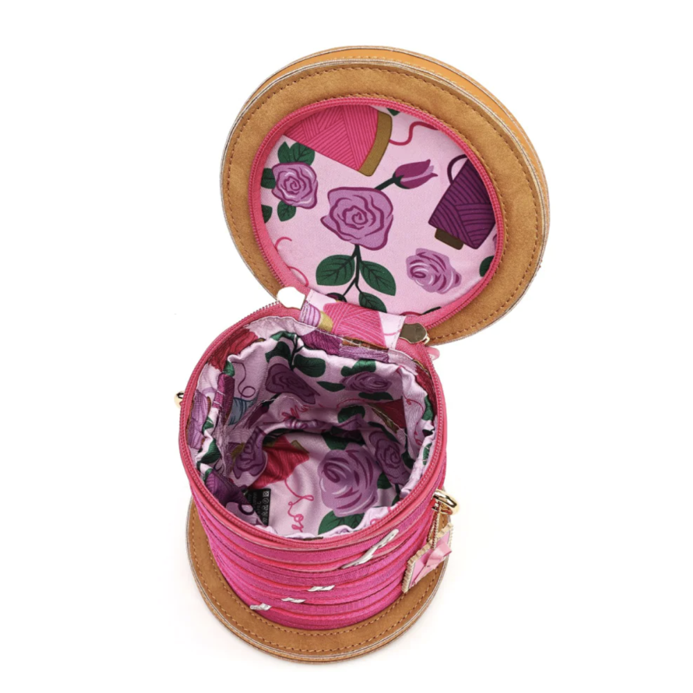 A round pink and tan bag shown open, revealing a floral-patterned interior with pink, purple, and green rose motifs.