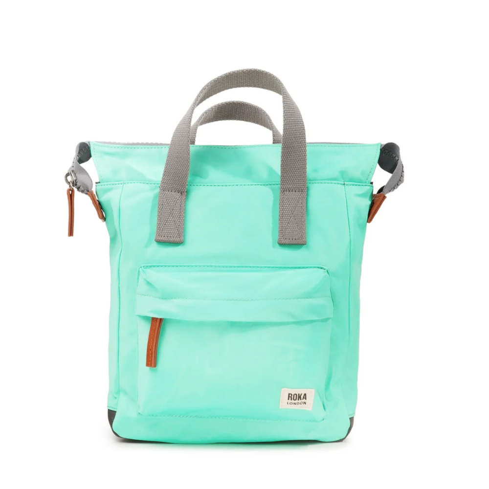 A light blue Roka Bantry B recycled nylon small backpack with a front pocket, two side handles, and a vegan pull zipper.